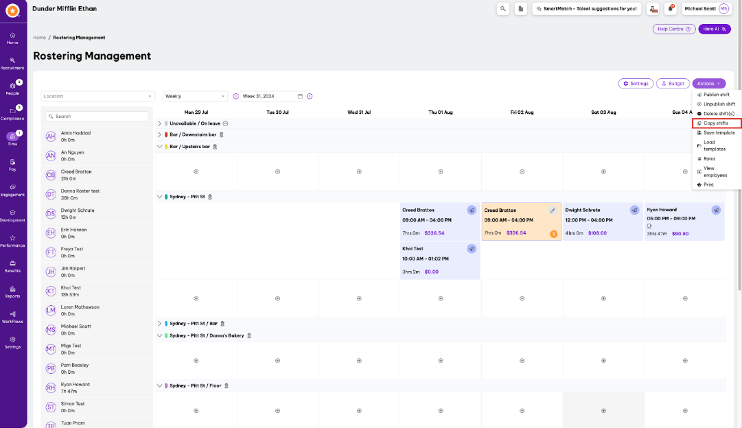 Roster management interface for Dunder Mifflin Ethan, showing a weekly view of employee shifts. The left panel lists employee names and their assigned hours, while the main schedule displays shifts for each day with details like time, hours, and wages. Controls at the top allow for filtering by location and week selection. Options in the 'Actions' menu include 'Publish shift,' 'Unpublish shift,' 'Delete shift(s),' 'Copy shifts,' and more. Settings and Budget buttons are also accessible.